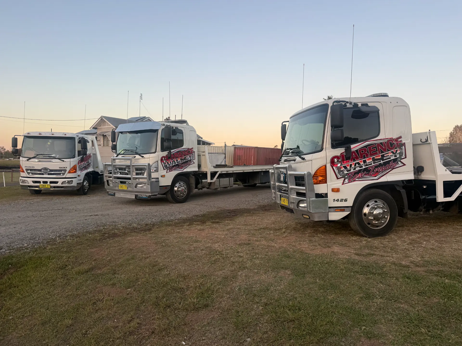 Three tow trucks lined up nose-on at the depot in evening light